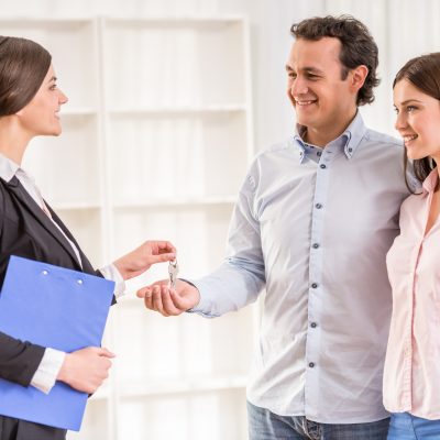 Female realtor is giving to young couple a key from new flat.